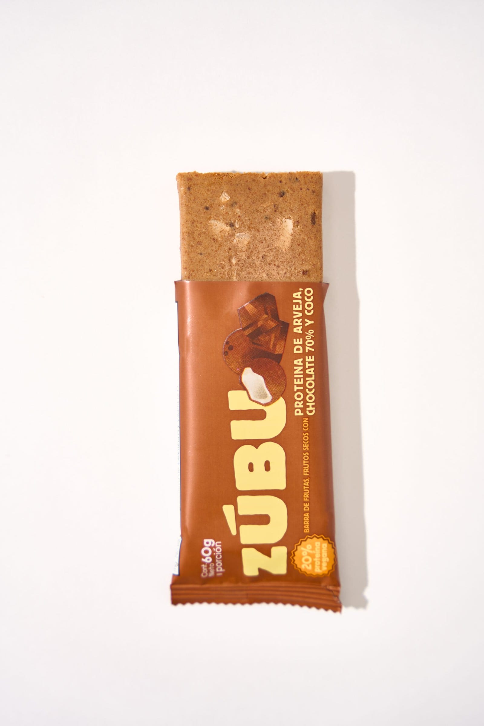 Una barrita de proteínas Zúbu, con arveja, chocolate 70% y coco, parcialmente desenvuelta, sobre un fondo blanco con su distintivo envase.