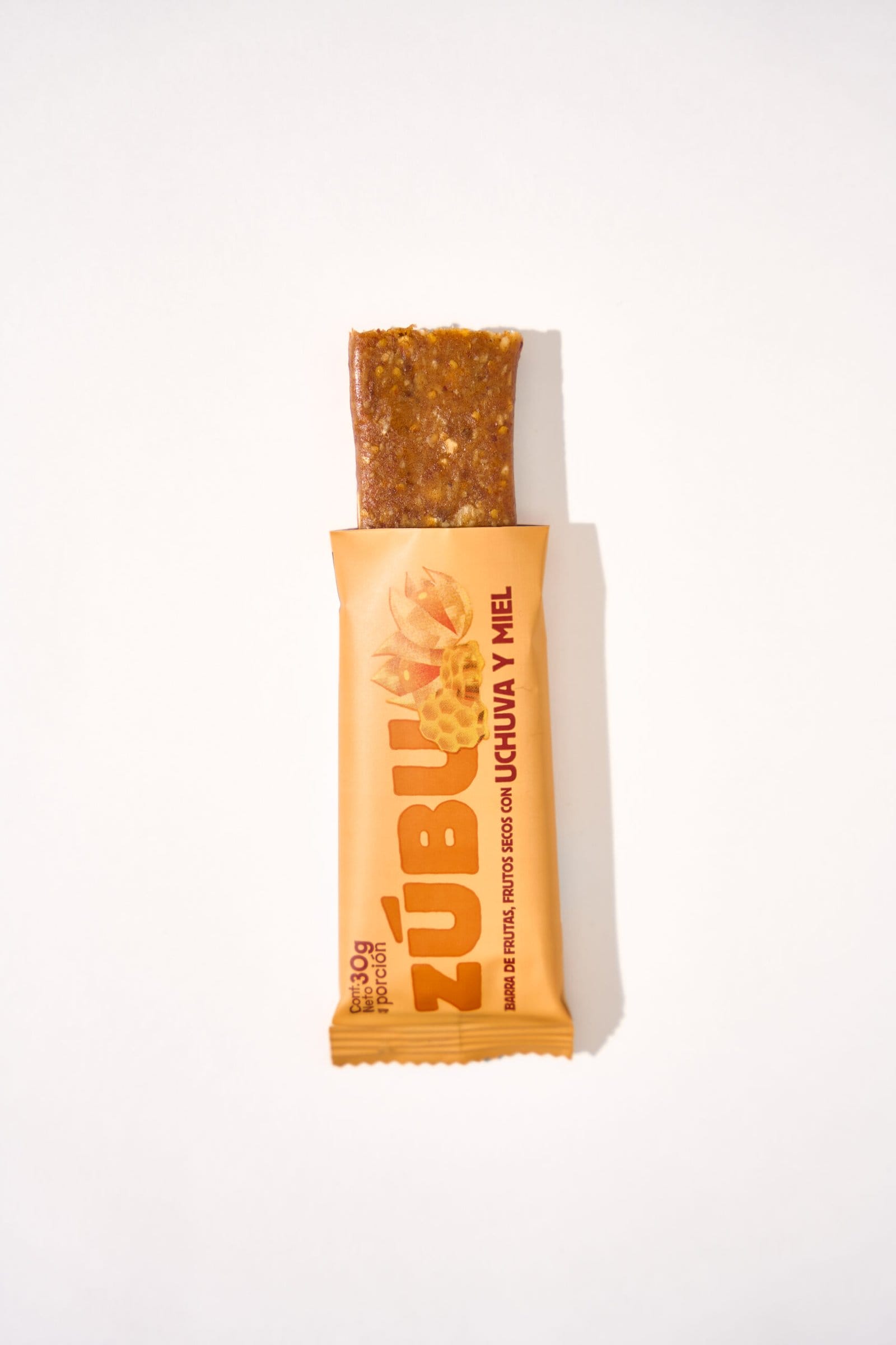 Una barrita parcialmente desenvuelta de con arveja, chocolate 70% y coco con semillas de chía visibles, miel y un toque de chocolate, colocada sobre un fondo blanco liso.